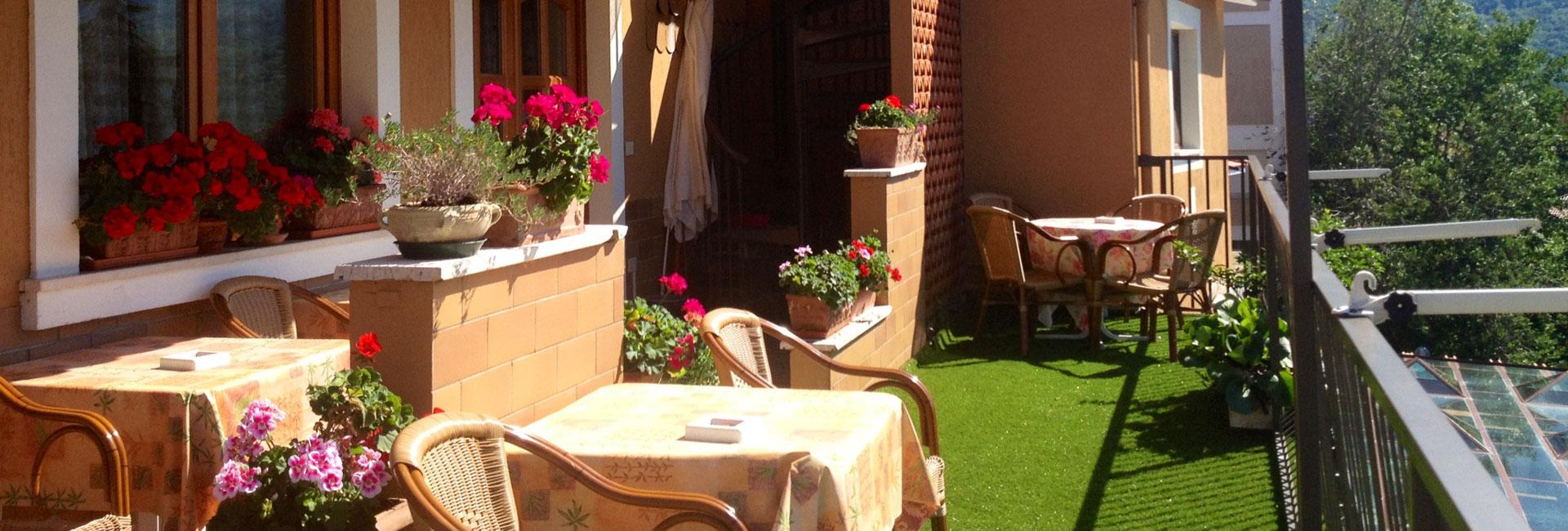 Terrazza con tavolini, sedie e fiori colorati su prato sintetico.