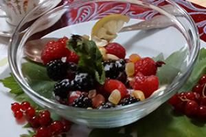 Frutti di bosco in una ciotola di vetro con decorazione di foglie e limone.