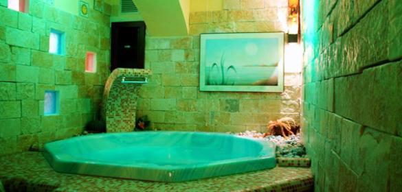 Vasca idromassaggio in ambiente rilassante con luci soffuse e pareti in pietra.