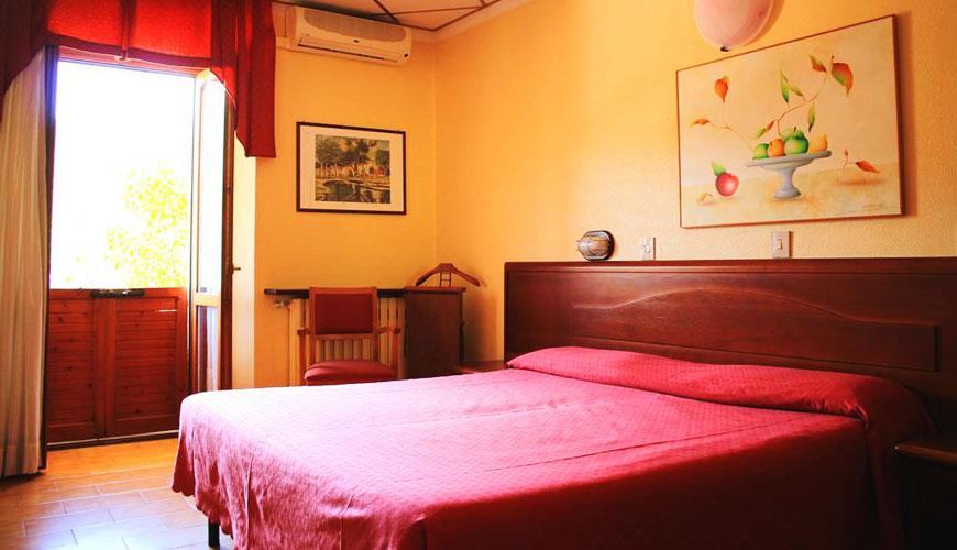 Camera da letto con letto matrimoniale, arte colorata e luce naturale da porta aperta.