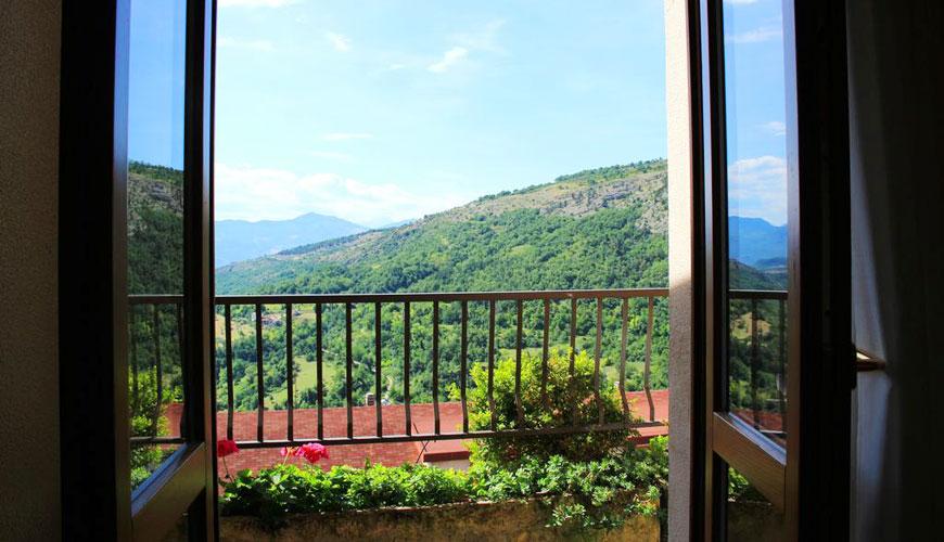Vista dalla finestra su colline verdi e cielo azzurro, con fiori sul balcone.